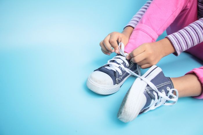 a little girl with Dyspraxia tying a pair of tennis shoes 