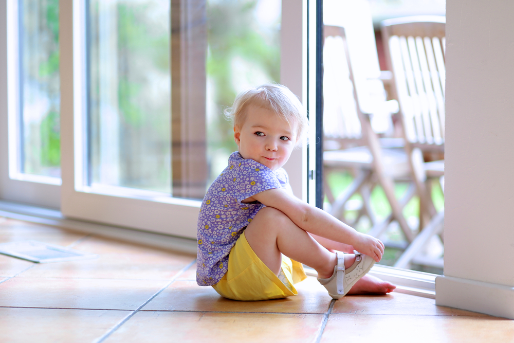 a little girl sitting on the floor in front of a sliding glass door holding her foot