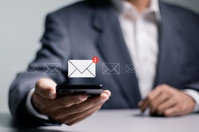 a man in a suit holding a cell phone with an email icon on it