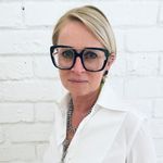 a woman wearing glasses standing in front of a brick wall