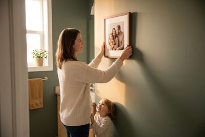 a woman and a little girl hanging a picture on a wall