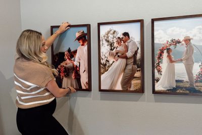 A woman putting up frames on her bedroom wall.