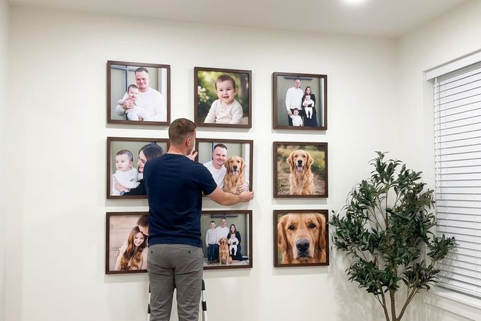 11 Gallery Wall Layout Ideas for a Flawless Display A man hanging up maple framed portraits.