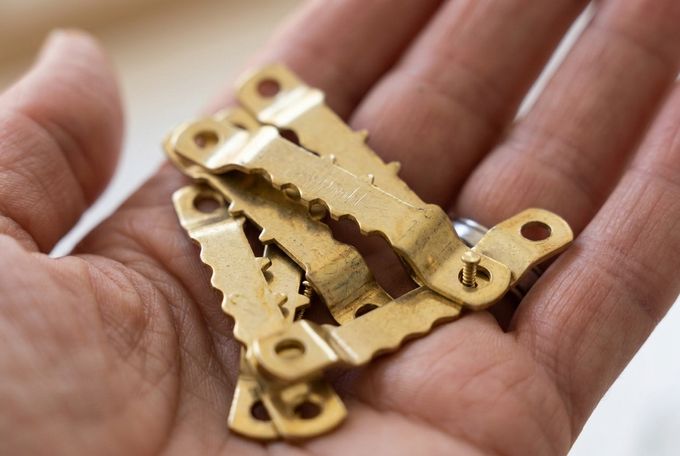 a hand holding brass sawtooth picture hangers in it's palm