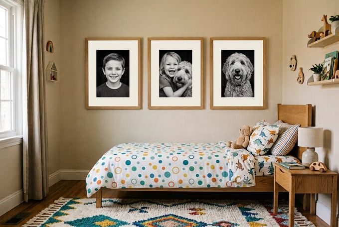 Three large oak frames with black and white sibling portraits above a linen-dressed bed on a sage-green wall
