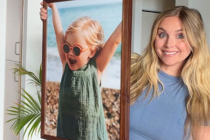 A woman holding up a wooden picture frame.