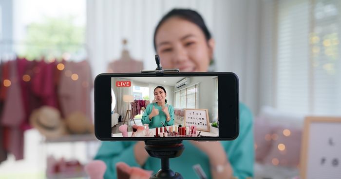 Video marketer filming herself making a makeup product demo video on her cellphone