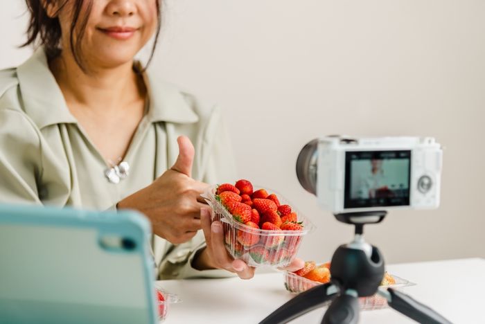 Woman making sales video with strawberries and video camera for her online store
