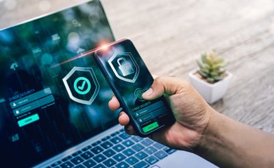 a person holding a cell phone in front of a laptop with cybersecurity