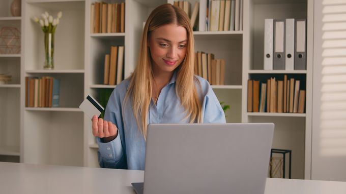 A woman holding a credit card and looking at a laptop .