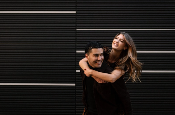 A man hugging a woman in front of a black wall.
