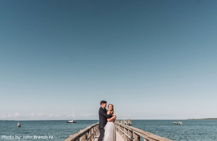 A bride and groom standing on a pier by the ocean. Photo by: John Branch IV