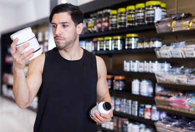 a man holding a creatine supplement in a store thinking about the myths and misconceptions of taking creatine supplementation for health and athletic performance