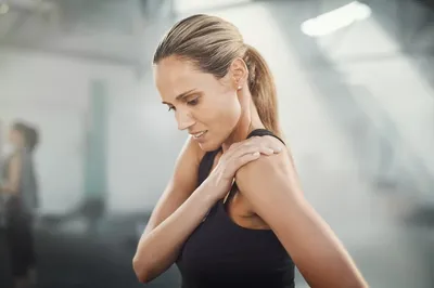 a woman in a black tank top holding her shoulder as she feels soreness and inflammation 