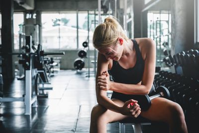 a woman sitting on a bench in a gym: Discover Best Pain Reliever for Sore Muscles After Workout 