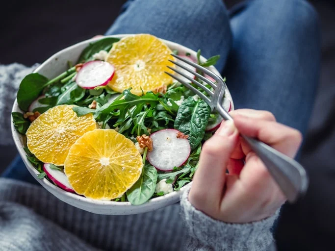 a person holding a bowl of salad rich in iron with oranges, nuts, and radishes