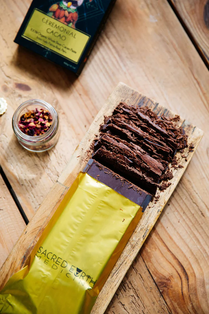 A Sacred Earth Medicine Ceremonial Cacao 5kg Block being chopped up on a wooden table.