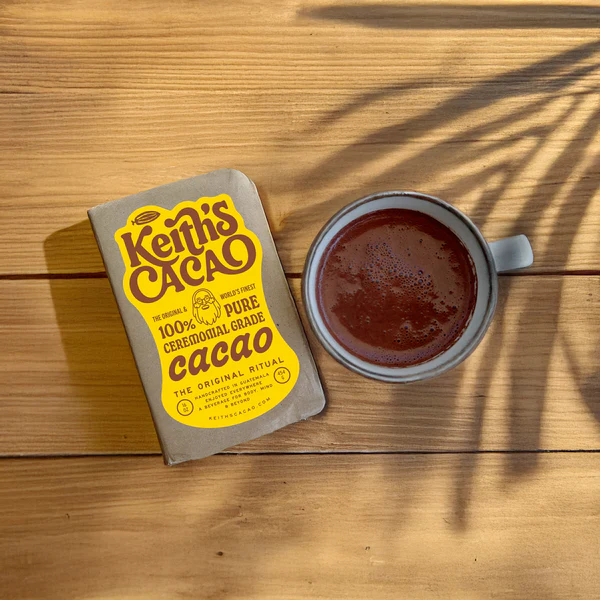 A cup of cacao next to a brick of Keith's Cacao Ceremonial Cacao on a wooden table