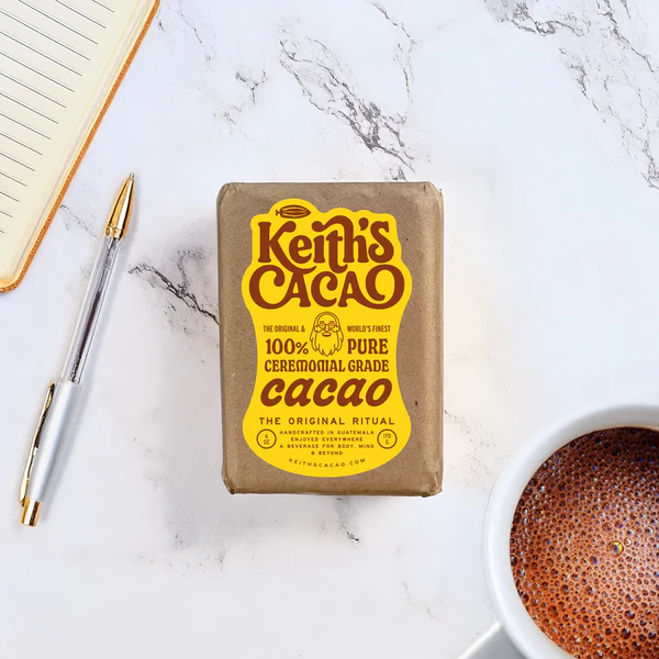 A cup of cacao next to Keith's Cacao Ceremonial Cacao Mini Brick.