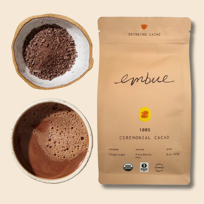 A bag of Embue Ceremonial Cacao Drinking Cacao next to a cup of Cacao.