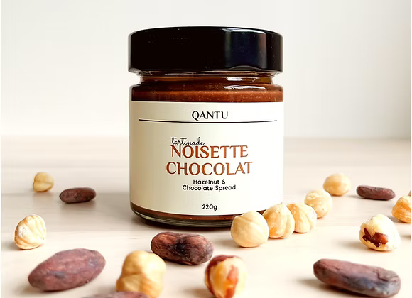 A jar of chocolate hazelnut spread surrounded by nuts and cacao beans.