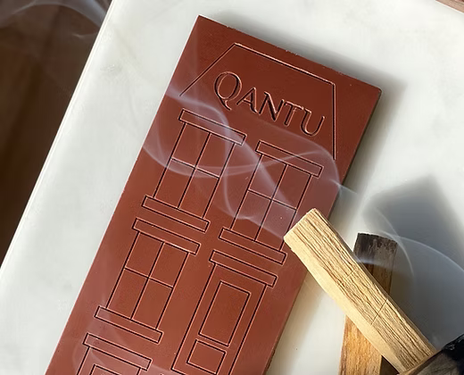 A piece of chocolate sitting on top of a table, with a stick of Palo Santo burning next to it.