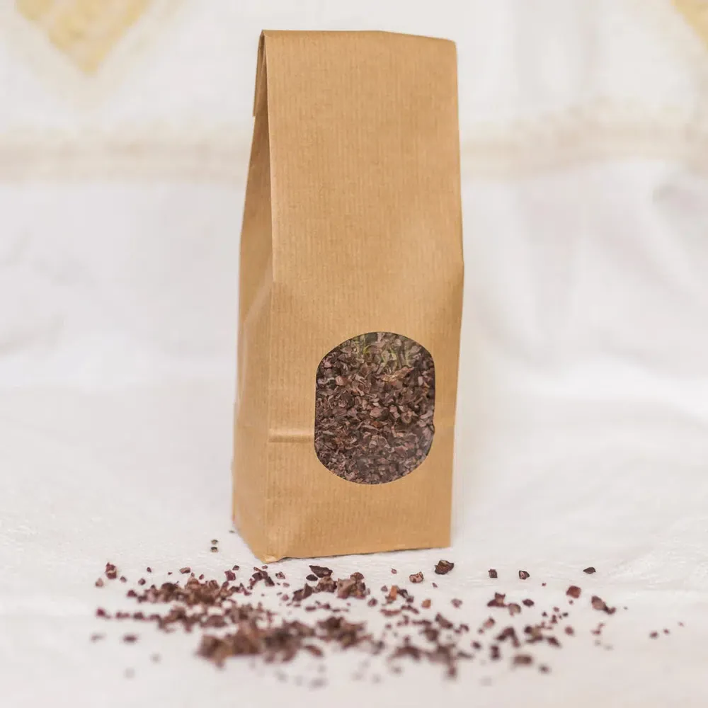 A brown paper bag filled with Herbal Cacao Ceremonial Cacao Nibs.