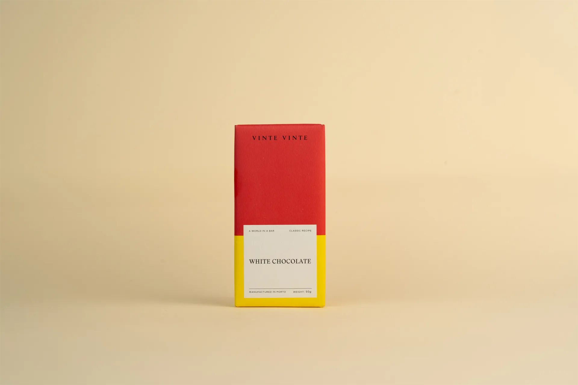 A slab of Vinte Vinte White Chocolate. The packaging is red and yellow, and the bar is sitting on top of a table.