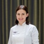 a woman in a chef coat standing in front of a curtain