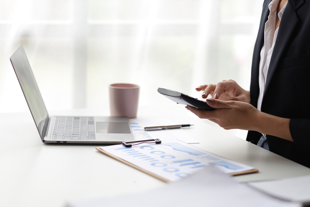 Woman sitting in front of a laptop while working on a calculator and checking data on a spreadsheet