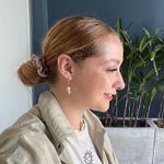 Martine Smit smiling in profile, wearing a pearl earring and khaki jacket, with green plants and a navy wall behind her