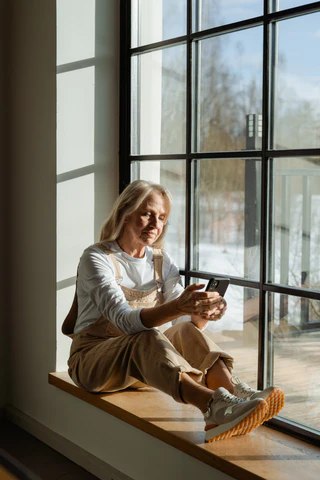 a woman sitting on a window sill looking at her cell phone