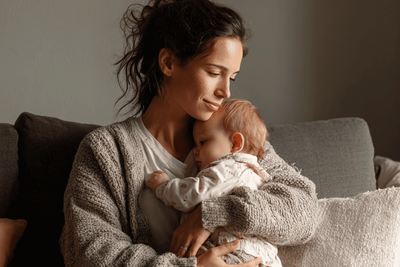 A new mom holding her baby, while feeling the effects of loose pelvic floor muscles.