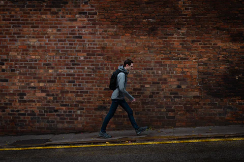 a man walking down a street past a brick wall