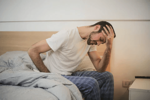 Chronic Pelvic Pain Syndrome A man sitting on the edge of a bed in pajamas, holding his head in distress