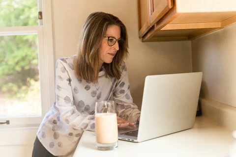 a woman sitting at a kitchen counter using a laptop computer
