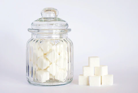 a glass jar filled with sugar cubes next to a pile of cubes