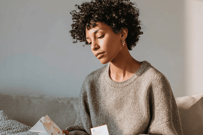 A woman sitting on a couch deciding on a pelvic floor trainer to use.