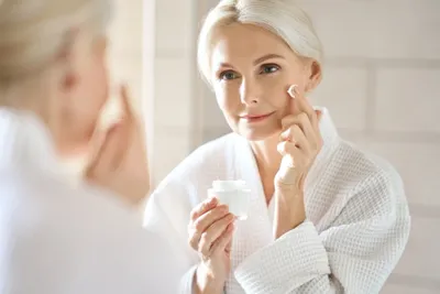 A woman applying retinol to her face to reduce wrinkles.