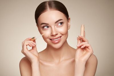 A woman holding a concealer to apply to her face.