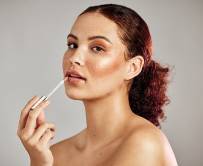 A woman holding a lip gloss brush to her mouth
