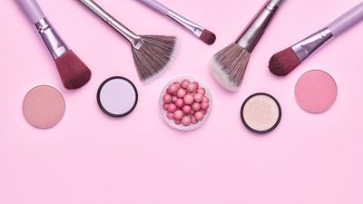 A collection of makeup brushes and powders on a pink background.