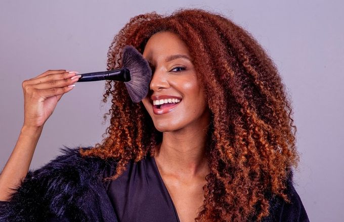 A woman holding a makeup brush to her face.