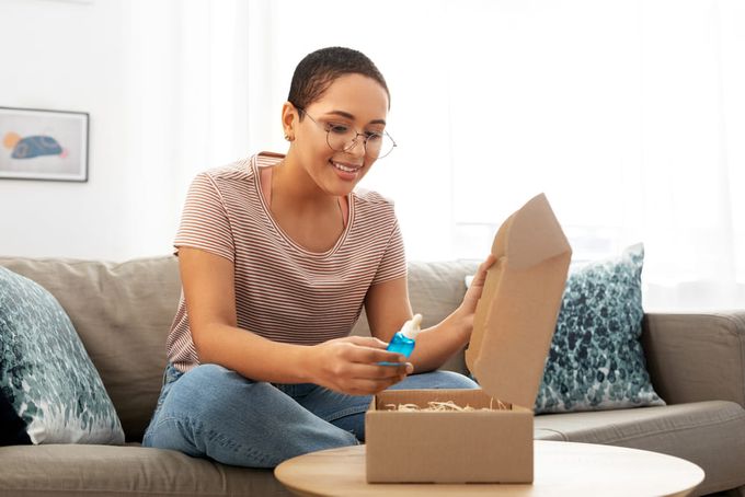 A woman sitting on a couch opening a beauty box.