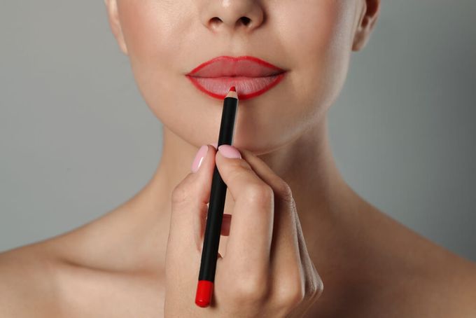 A woman with red liner around her lips holding a black lip pencil