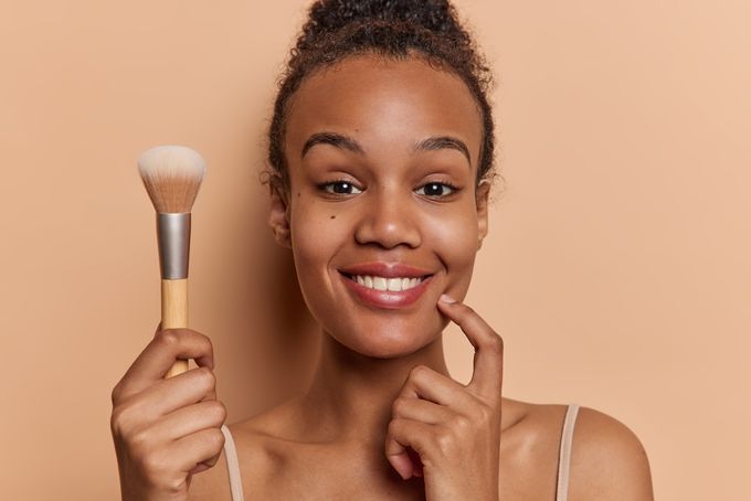 A woman holding a makeup brush and smiling.