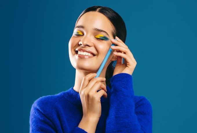 A woman smiling while holding a makeup brush to her ear.