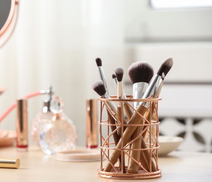 A set of makeup brushes in a copper holder.