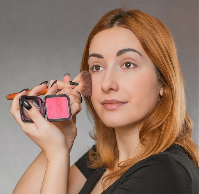 A woman holding a makeup brush and a blush in her hand.