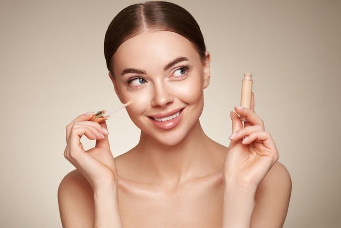 A woman holding a concealer to apply to her face.